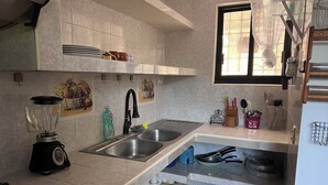Uma cozinha com fogão a gás, pia, liquidificador e janela com cortina.