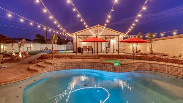 Un jardin avec une piscine, des parasols, des guirlandes lumineuses et un espace salon abrité.