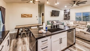 Une cuisine moderne dotée d’un îlot central, d’appareils électroménagers intégrés et de luminaires suspendus.
