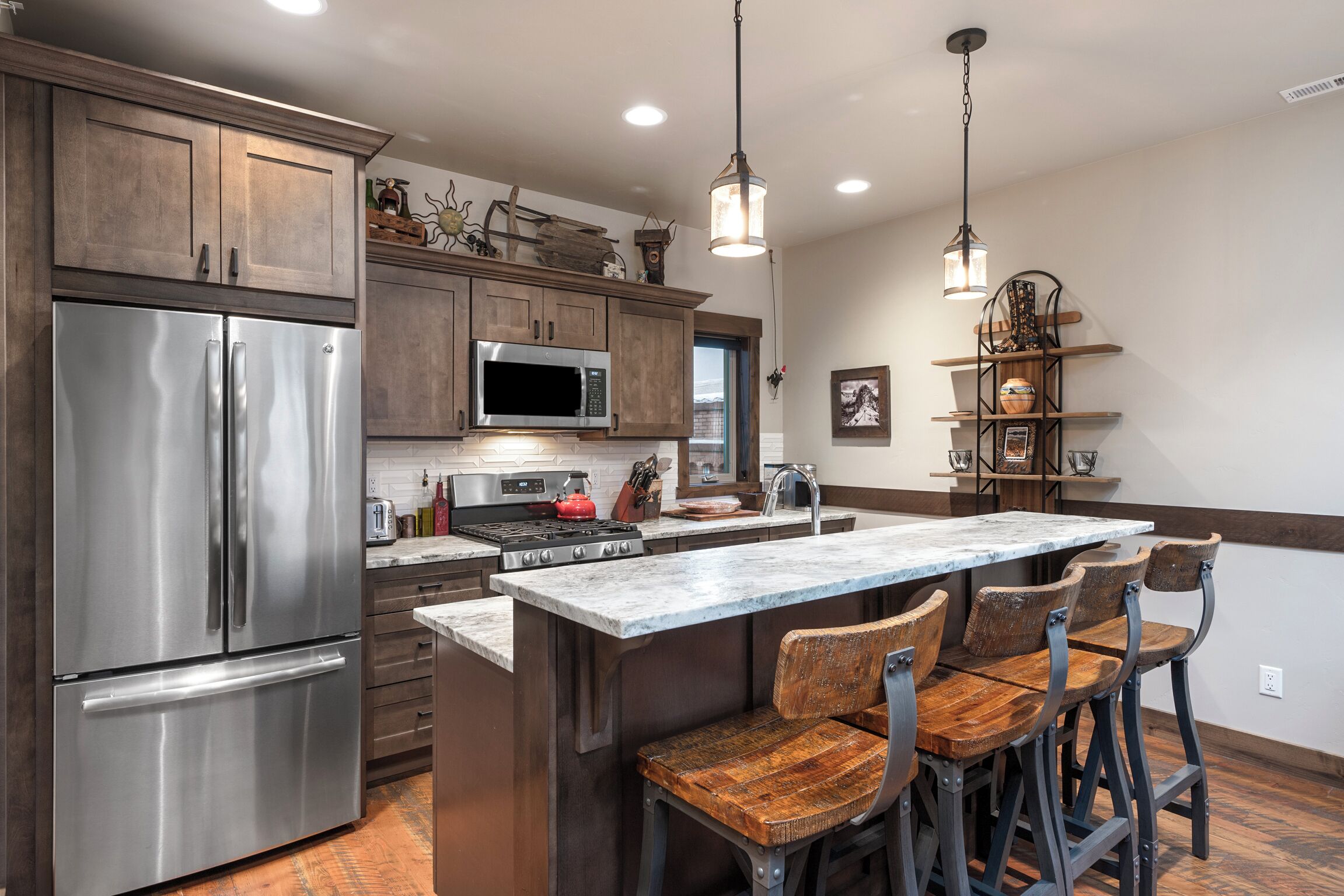 A kitchen with wooden cabinets, stainless steel appliances, a marble island, and bar stools.