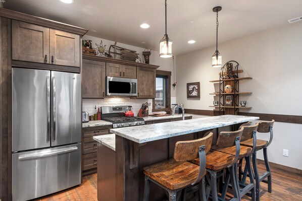 A kitchen with wooden cabinets, stainless steel appliances, a marble island, and bar stools.