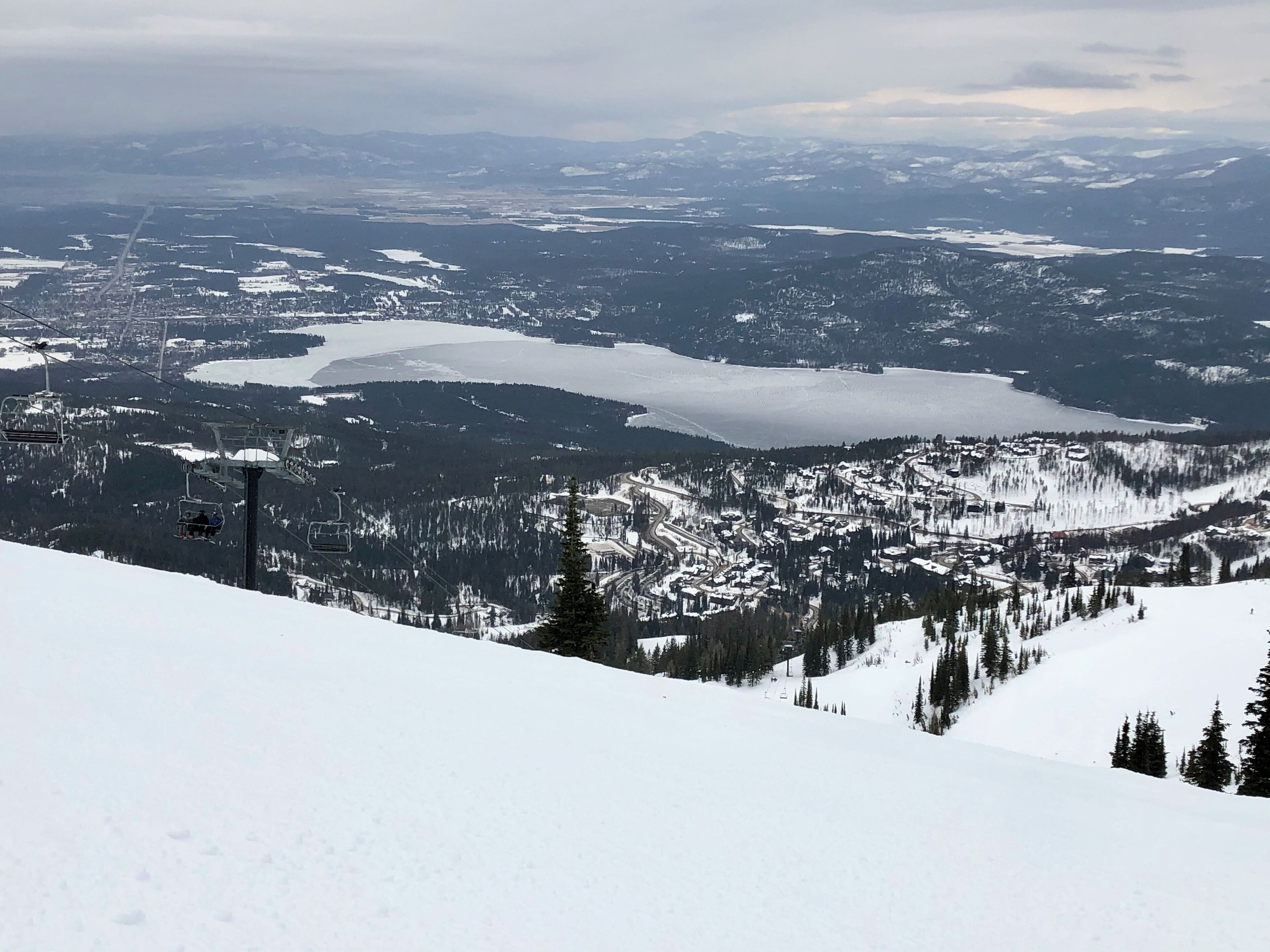 A snowy mountain landscape with a ski lift, a lake, and a town in the valley.