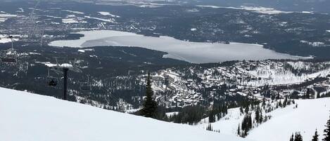 A snowy mountain landscape with a ski lift, a lake, and a town in the valley.
