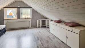 A room with a sloped ceiling, a radiator, a bed, a small table, and a cabinet with two pillows on top.