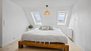 A bedroom with a wooden bed, white walls, a skylight, and a hanging light fixture. - Stunning apartment in Middelfart (Middelfart)