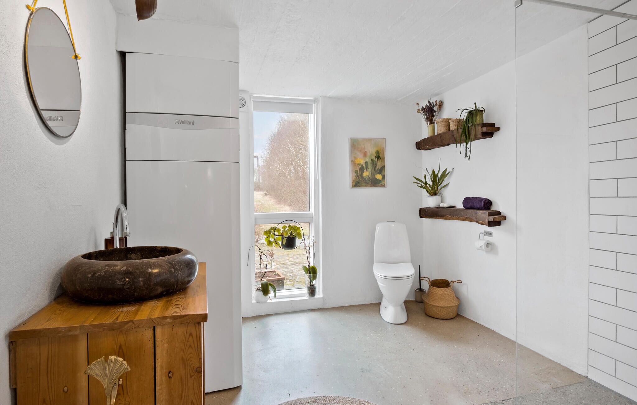 Een badkamer met een houten wastafelmeubel, een rond wastafel, een toilet en een raam met planten.