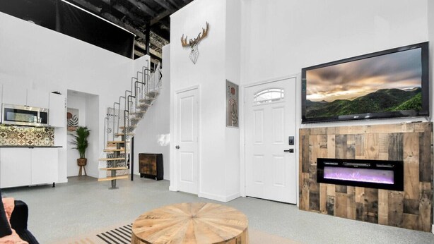 Un salon moderne avec un escalier, un téléviseur à écran plat fixé à un mur en bois et une table basse ronde en bois.