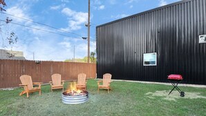 Un jardin avec un foyer, quatre fauteuils Adirondack et un barbecue.