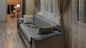 A room with a sofa, a small table, a chair, a window with curtains, and a hanging light fixture. - World Hostels (Baku)
