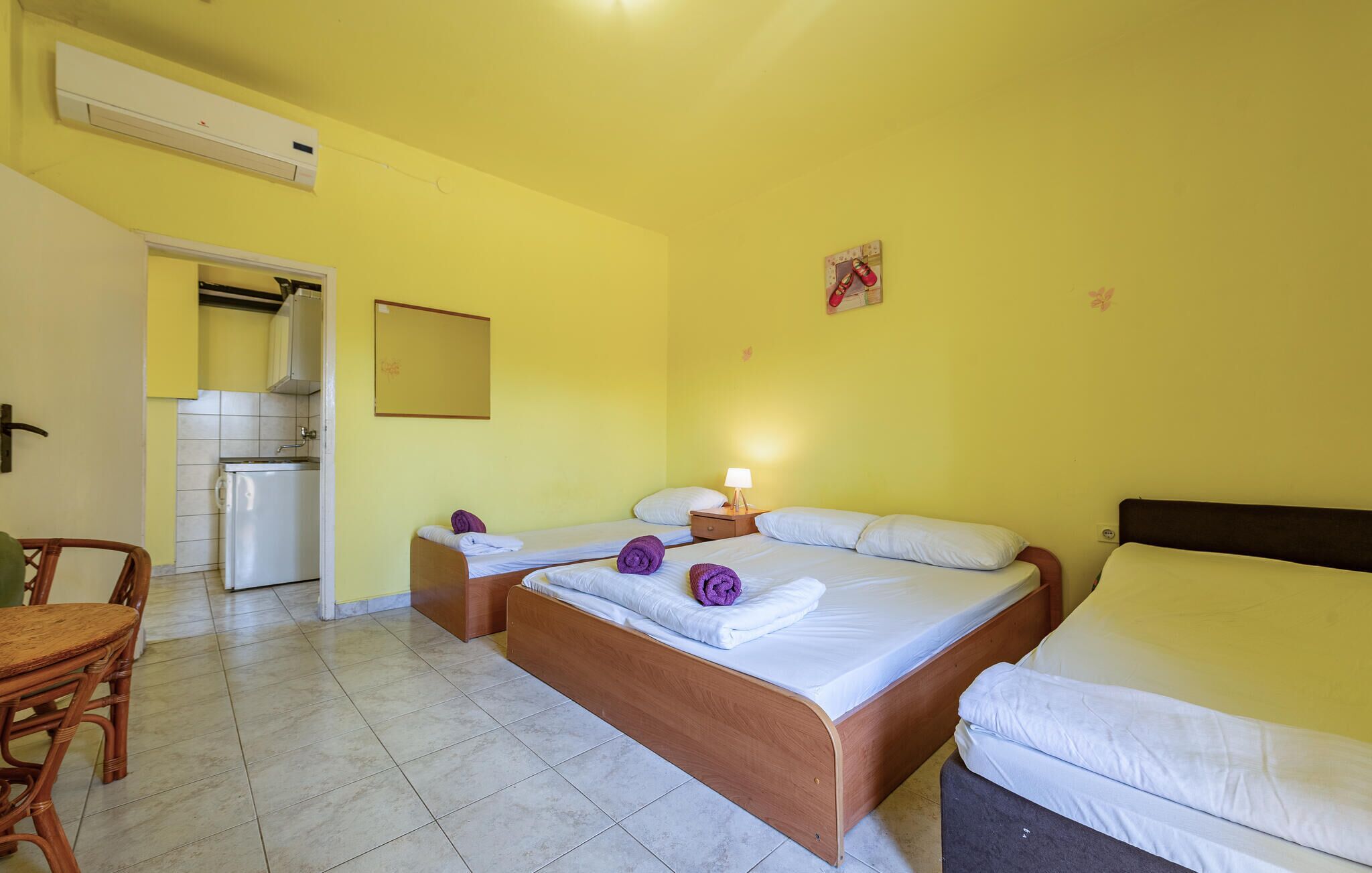 Una habitación de hotel con dos camas, una mesita y una kitchenette.