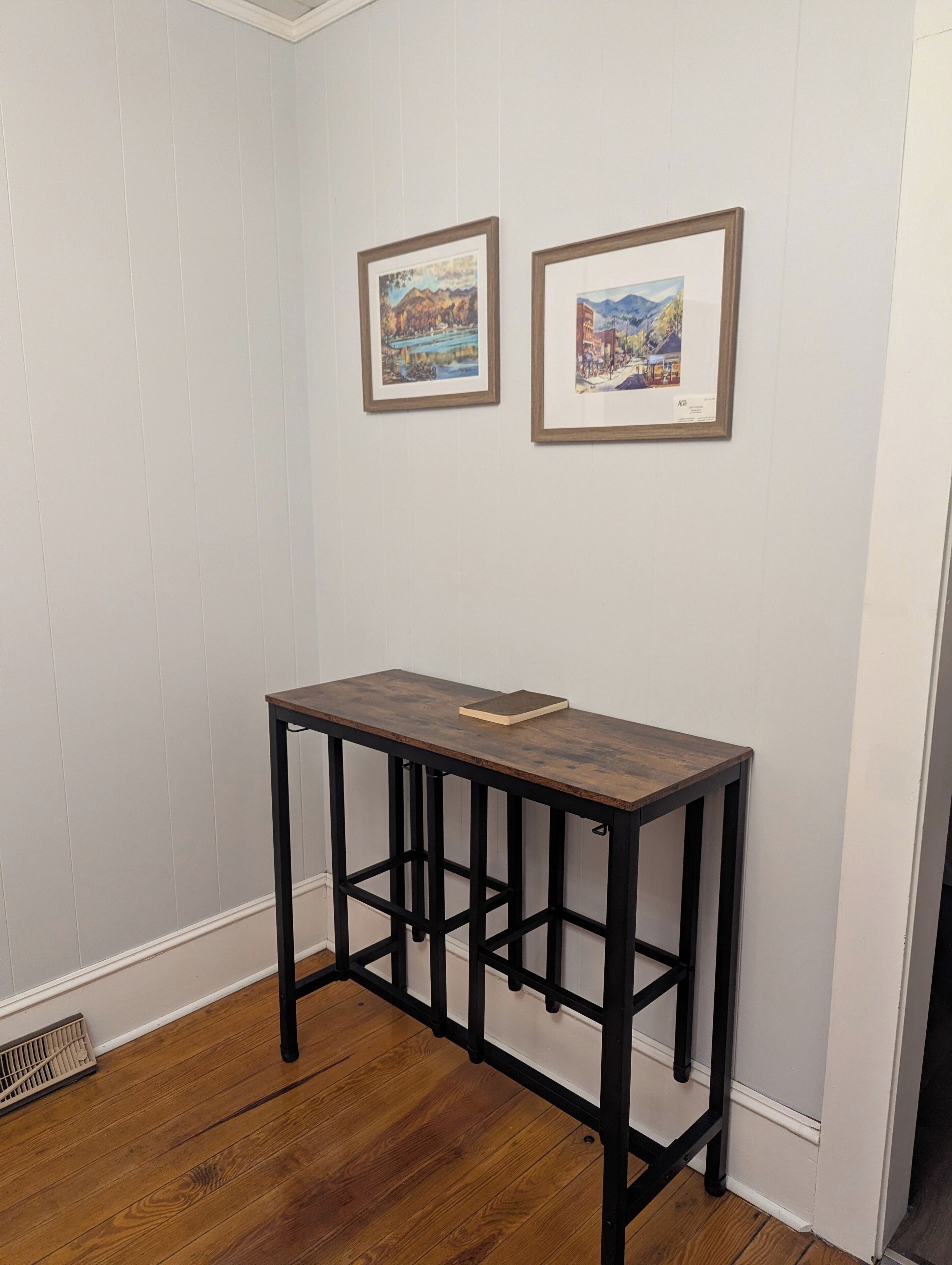 A room with a wooden table, white walls, and two framed pictures.