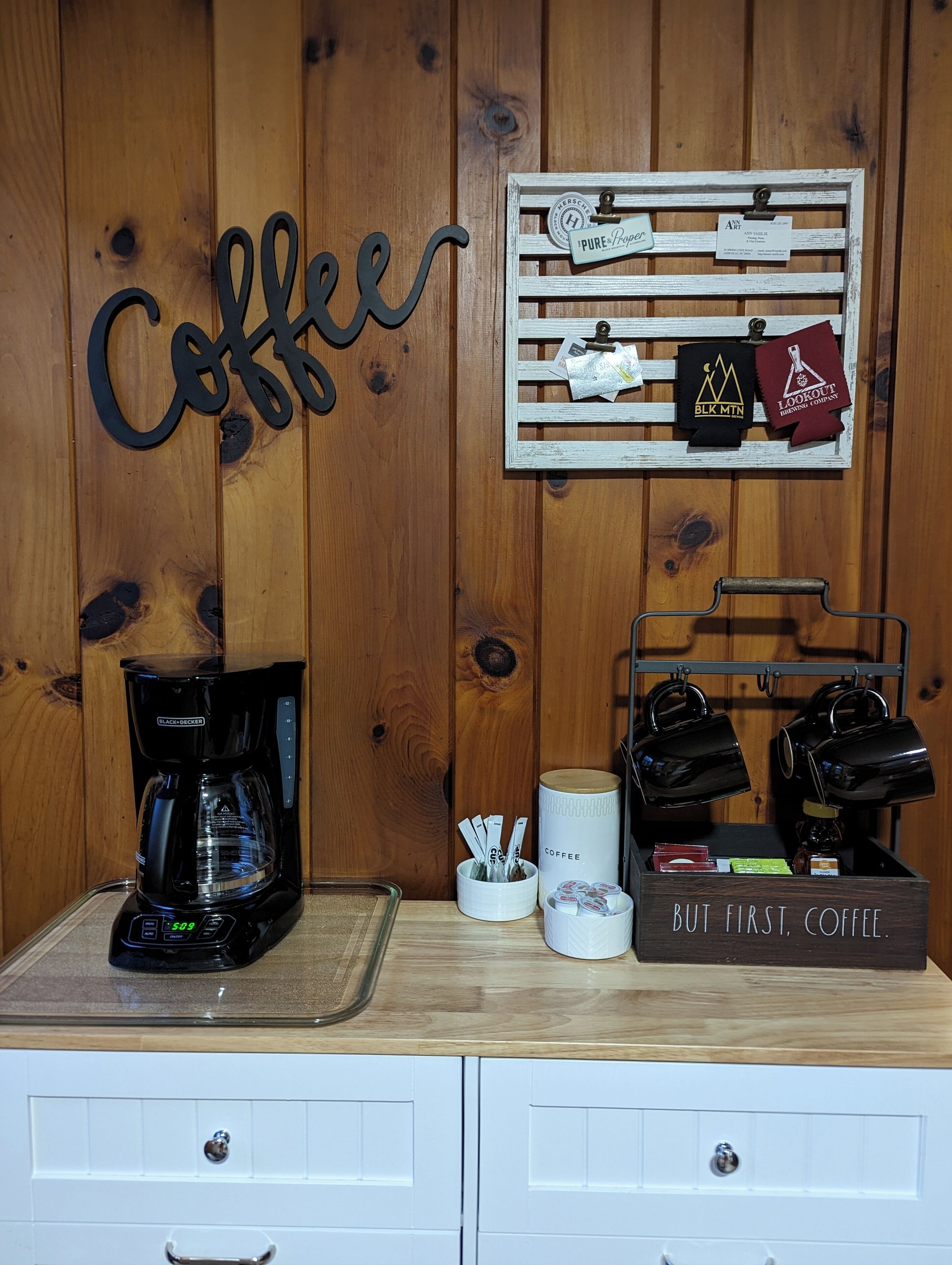 Een koffiehoek met een koffiezetapparaat, mokken en koffiecups op een houten toonbank.