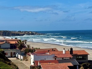 Zona residencial costera con casas de techo rojo, una playa de arena y el océano.
