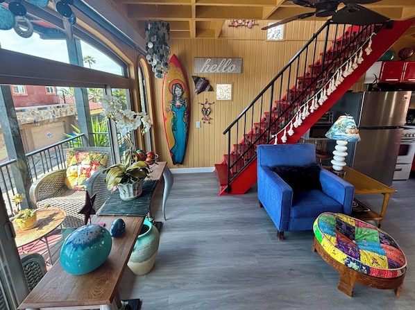 A cozy living area with a blue sofa, a colorful woven ottoman, a wooden coffee table, and a red staircase.