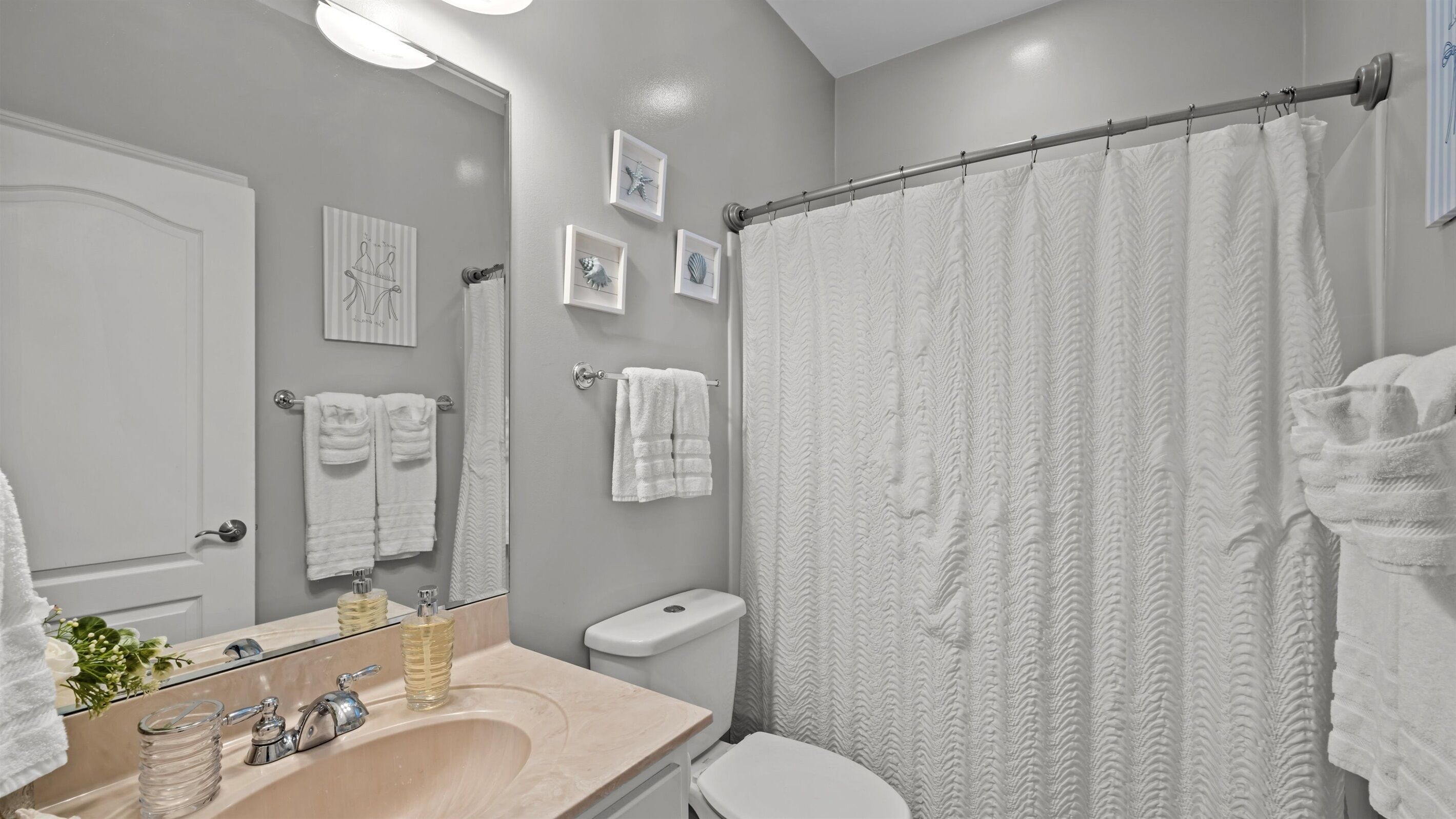 A bathroom with a beige sink, a mirror, a toilet, and a shower curtain.