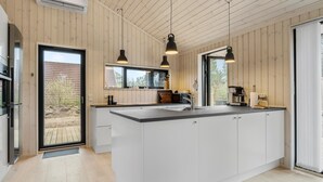 Une cuisine moderne avec des murs recouverts de panneaux en bois, un grand îlot central doté d’un évier et des luminaires suspendus.
