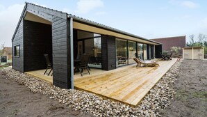 Une maison moderne dotée d’une terrasse en bois, d’un patio vitré et d’un espace salon extérieur.