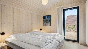 Une chambre à coucher avec un lit, un tableau, une lampe et une vue sur un immeuble, visible à travers une porte vitrée.