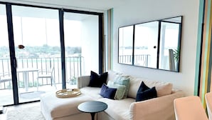 A living room with a sofa, a small round table, and a large window with a view of a balcony.