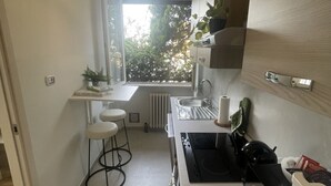 A compact kitchen with a window, a stove, a sink, and two stools. - Bnbook Trilo Buonarroti Pero (PERO)