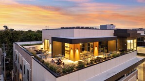A modern building with a rooftop terrace featuring outdoor seating and a glass-enclosed lounge area. - H&O on Music Row (Nashville)