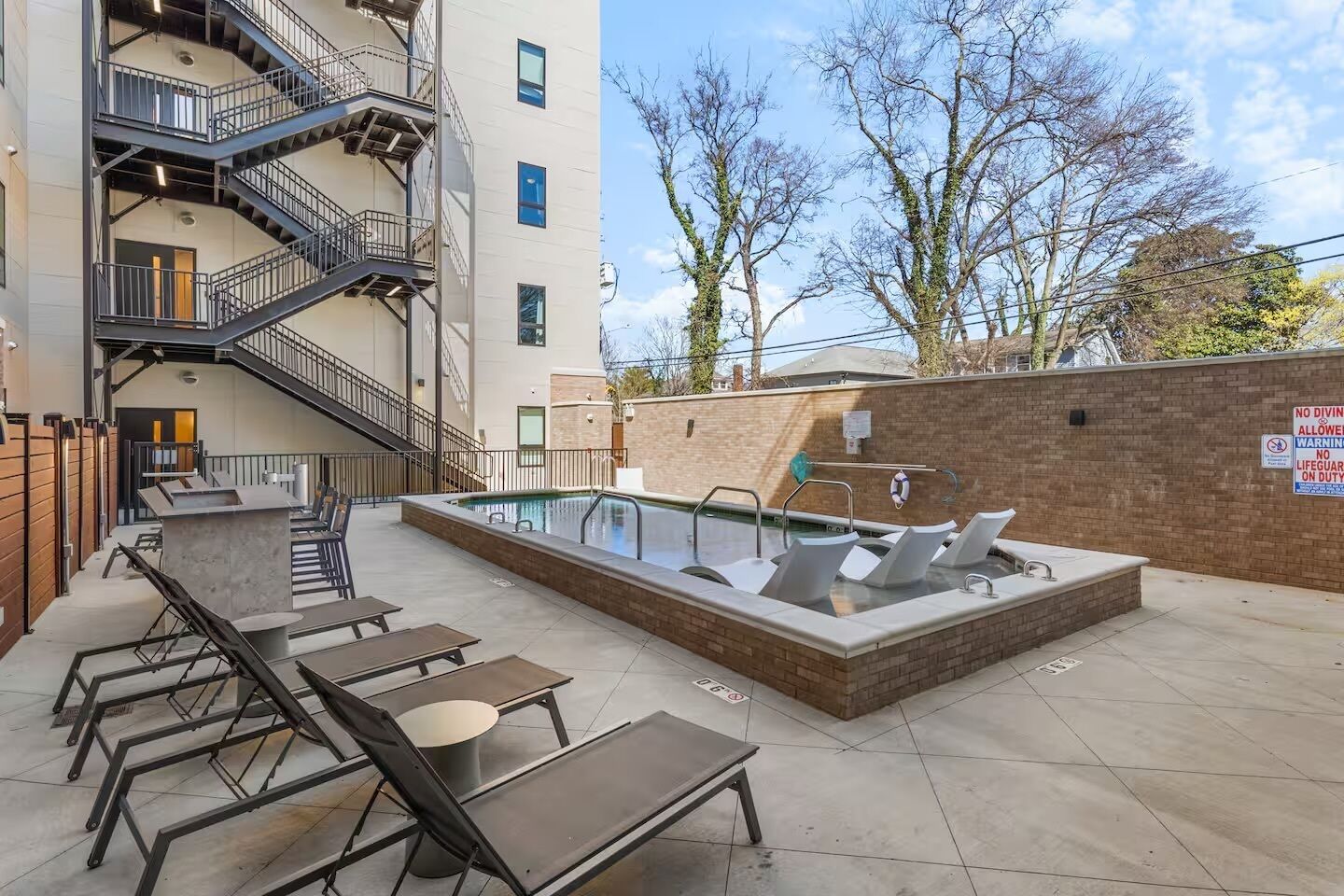 Un espace piscine aménagé sur le toit, comprenant un jacuzzi, des chaises longues et un escalier menant à un niveau supérieur.