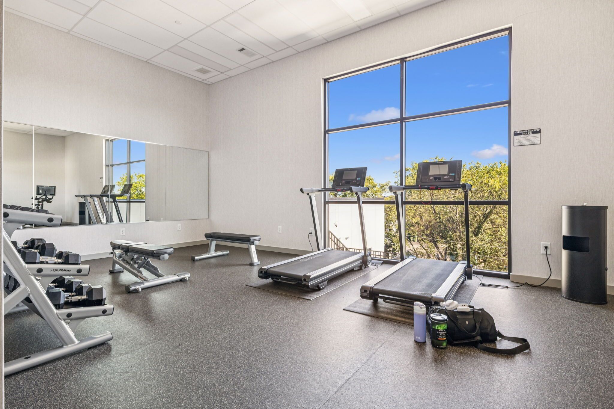 A gym with treadmills, weight machines, and a large window with a view of trees.