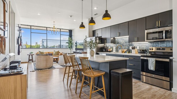 A modern kitchen with dark cabinets, stainless steel appliances, and a large island with bar stools. - H&O on Music Row (Nashville)