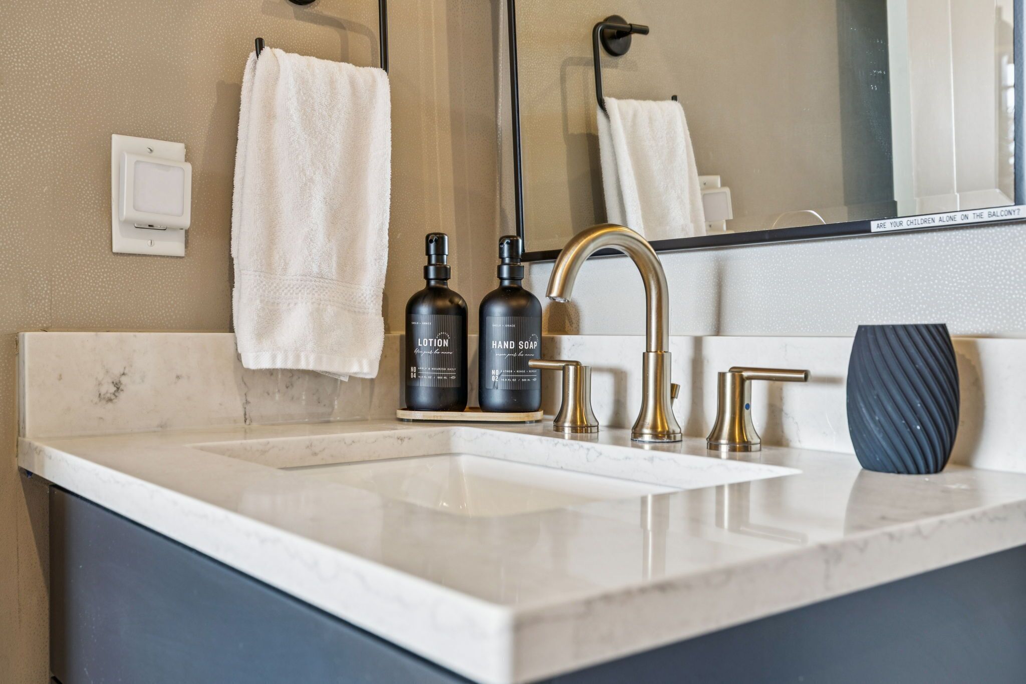A modern bathroom with a white sink, gold faucet, and two bottles of lotion.