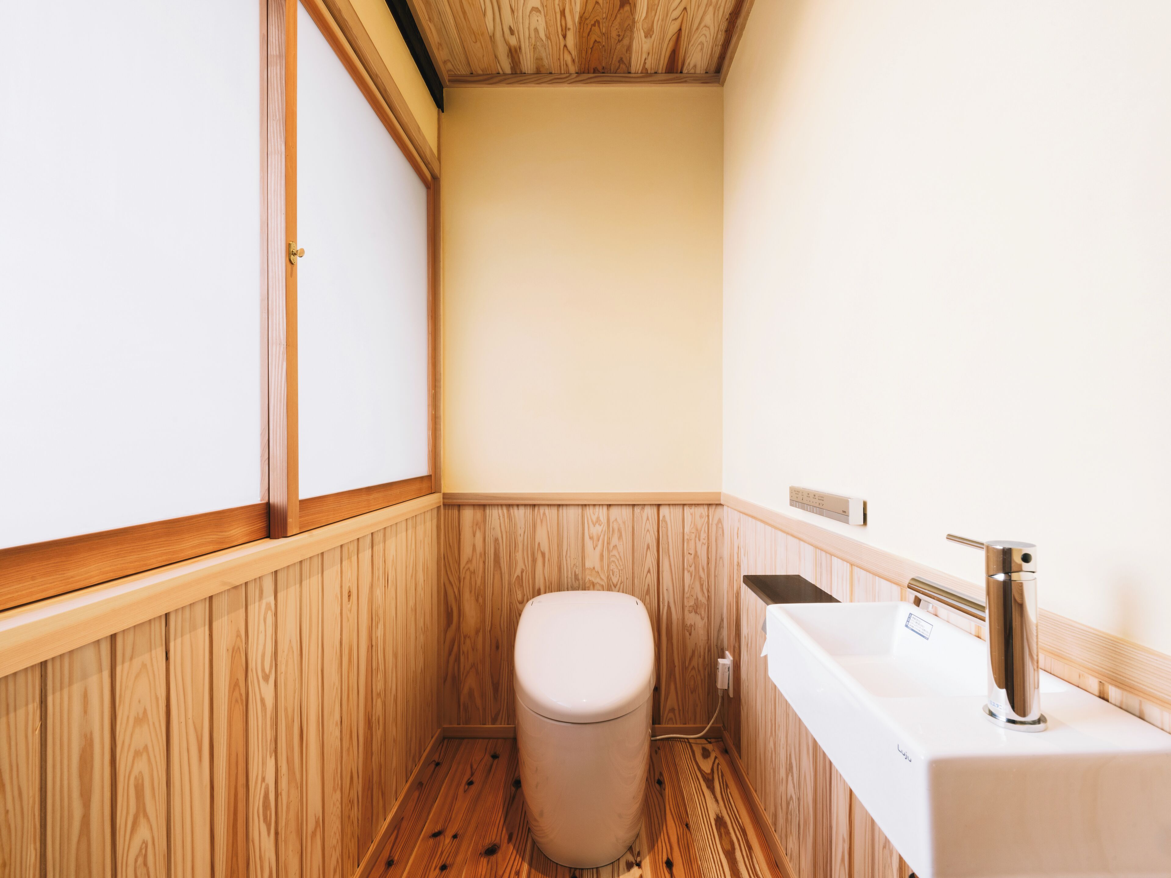 A compact bathroom with wooden paneling, a toilet, a sink, and a shower area.