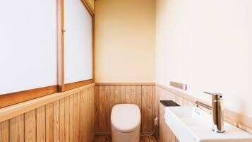A compact bathroom with wooden paneling, a toilet, a sink, and a shower area.