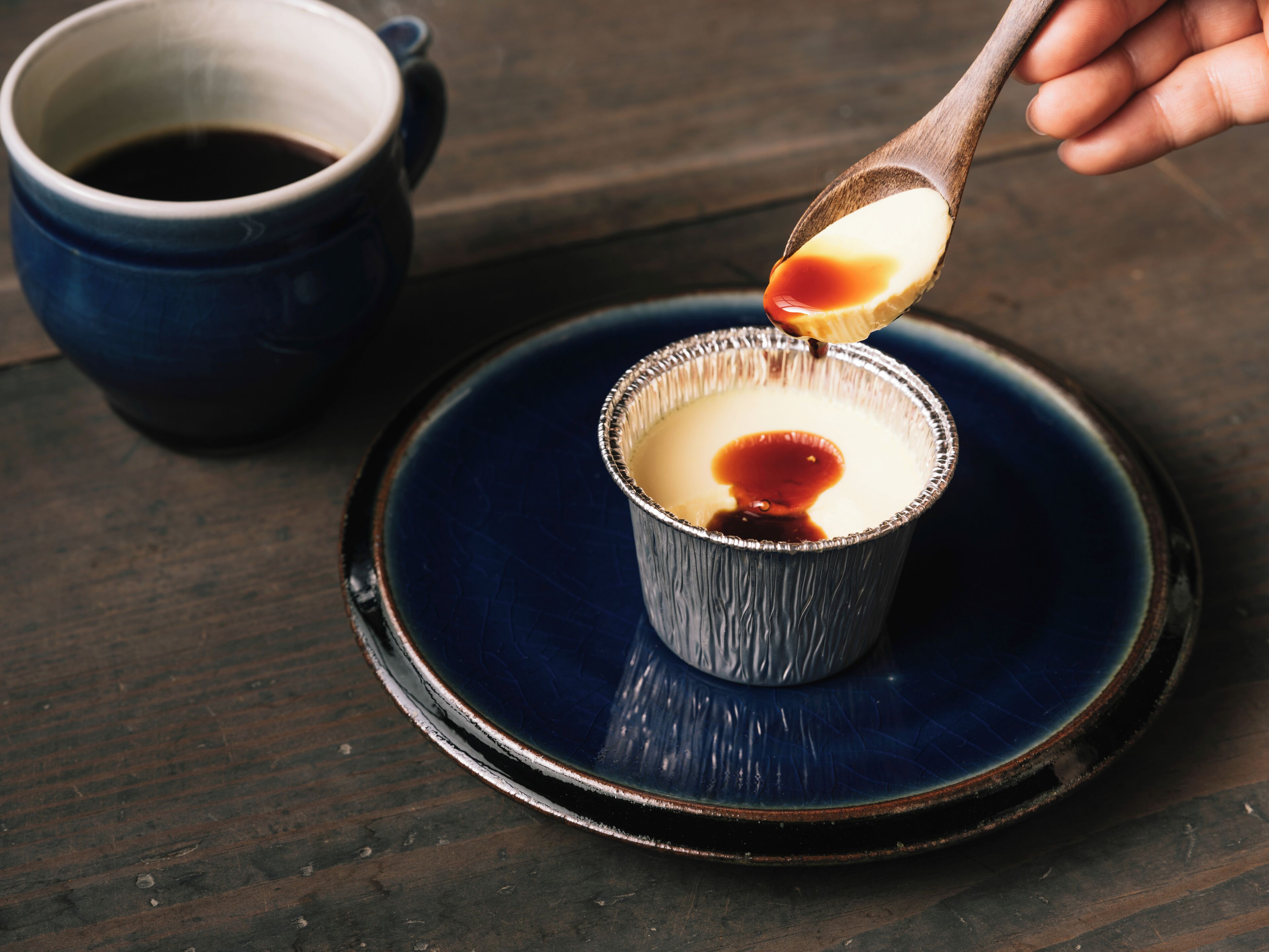 Een dessert in een foliebeker, met saus dat erin gegoten wordt, op een blauw bord geplaatst.