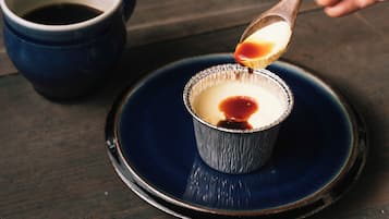 Un postre en vaso de papel aluminio, con salsa siendo servida con una cuchara, sobre un plato azul.