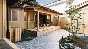 A covered patio area with a wooden deck, stone flooring, and a small garden with rocks and plants. - RITA Unnan Yoshida (Unnan)