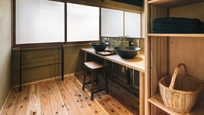 A compact kitchen with a wooden floor, a window with frosted glass, a sink, a stool, and a basket on a shelf. - RITA Unnan Yoshida (Unnan)