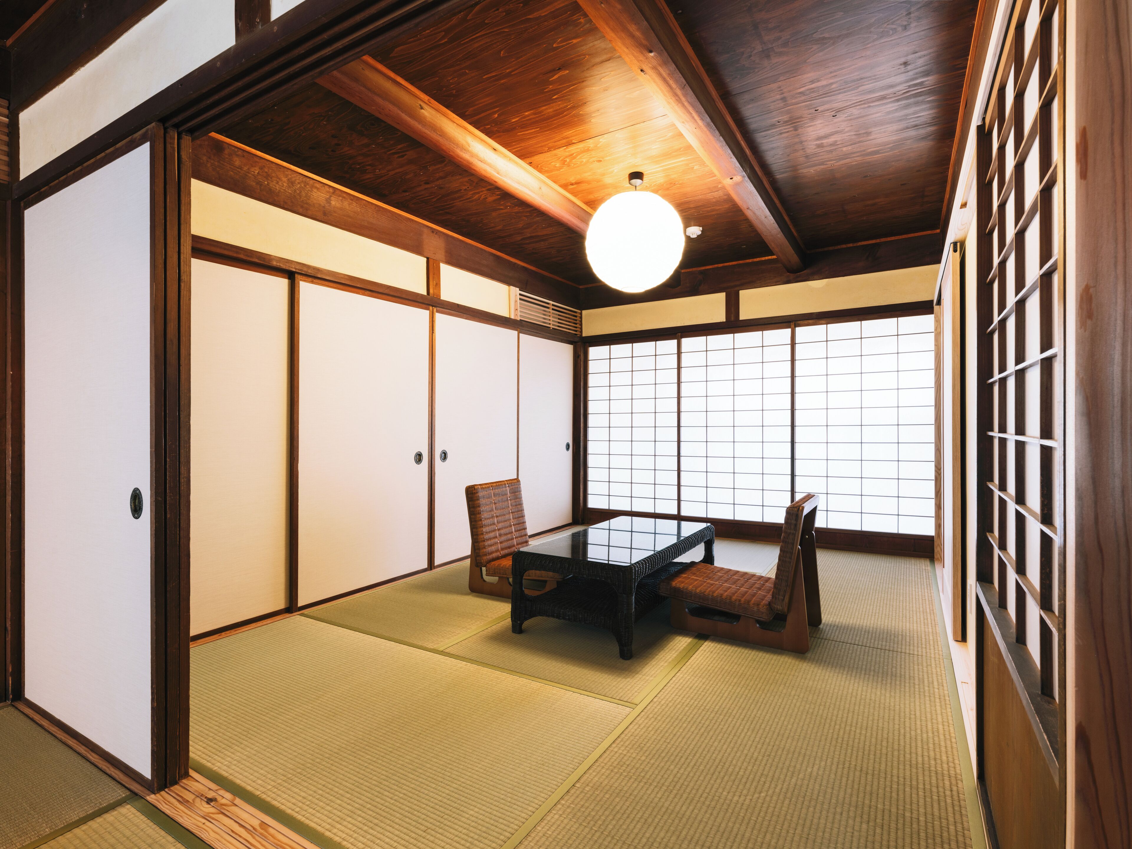 A traditional Japanese room with tatami flooring, sliding doors, and a low table with chairs.