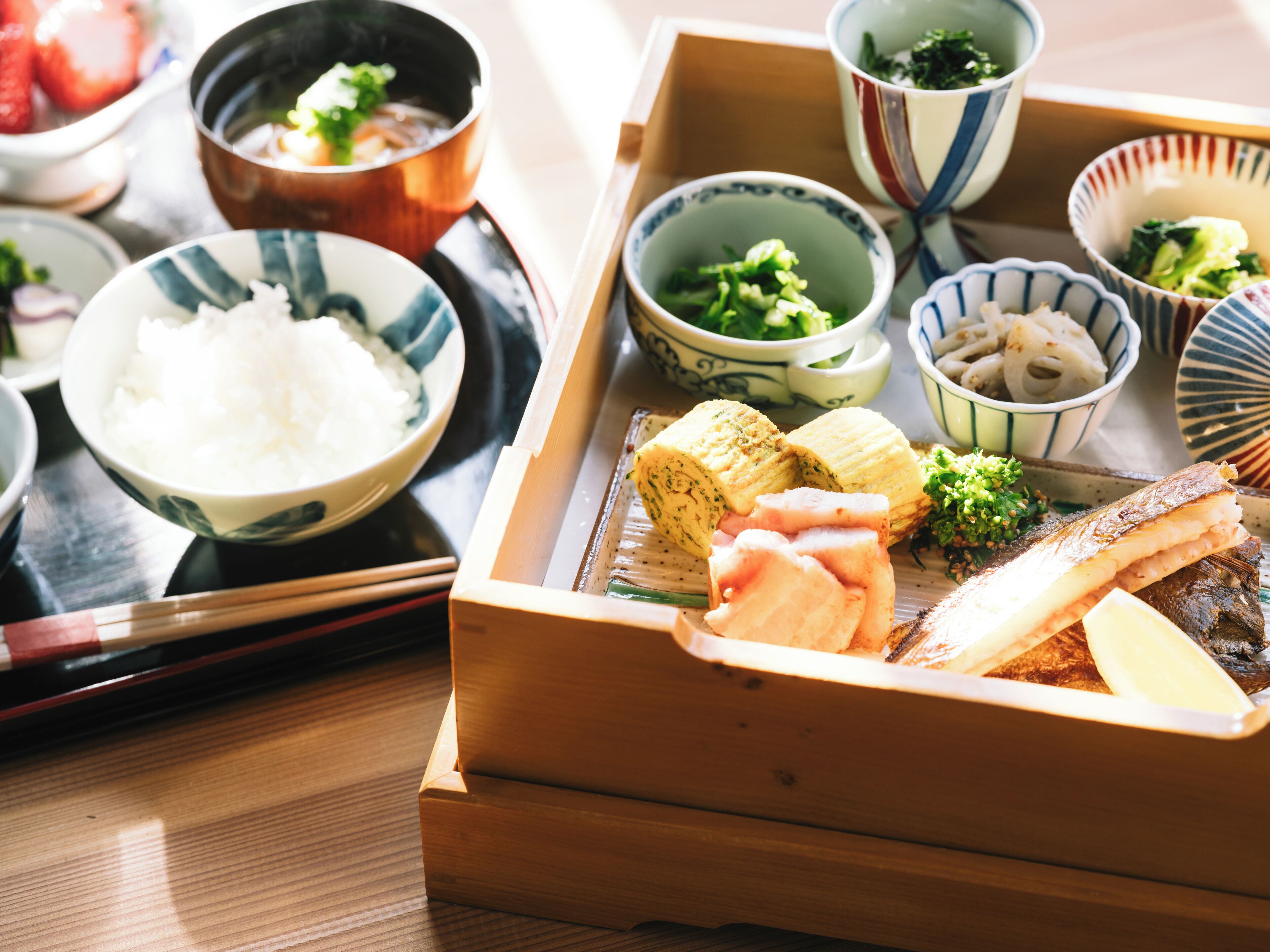 Comida japonesa tradicional con arroz, pescado y verduras servidas en una bandeja de madera.