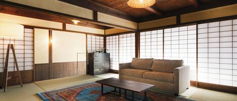 Une pièce de style japonais traditionnel, avec un sol recouvert de tatamis, une basse table en bois, un canapé et une grande fenêtre à panneaux coulissants (shoji).