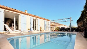 A swimming pool with a clear blue water surface, adjacent to a building with light blue doors and a tiled roof. - Lovely home in Lézignan-Corbières (Lézignan-Corbières)