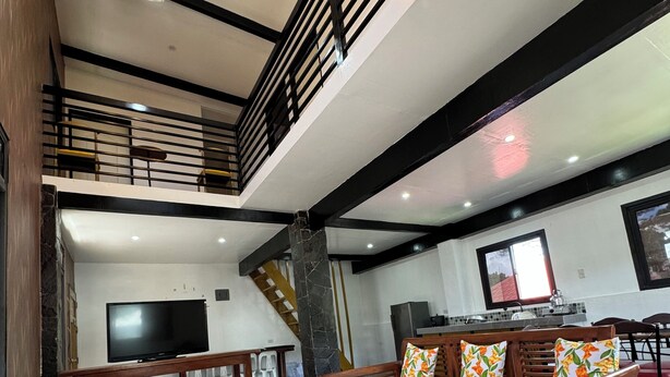 Un amplio espacio de sala con un sofá, una mesa de centro de vidrio y un televisor. Una escalera conduce a un nivel superior.