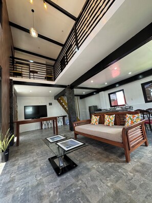 Un amplio espacio de sala con un sofá, una mesa de centro de vidrio y un televisor. Una escalera conduce a un nivel superior.