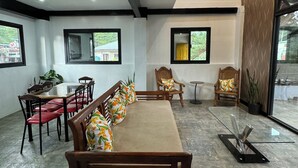 Una sala de estar moderna con sofá, mesa de comedor, sillas y una mesita de centro. Hay ventanas y vistas al exterior.