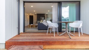 A modern living room with a sofa, two white chairs, a small table, and a glass door leading to a balcony. - The Ultimate 4-Bedroom City Escape (Christchurch)