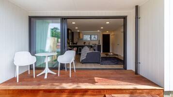 Eine moderne Terrassengrundstück mit Holzdeck, weißen Stühlen und einem kleinen runden Tisch.