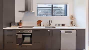 Eine moderne Küche mit dunklen Schränken, einem eingebauten Ofen, einem Geschirrspüler und einem Fenster über der Spüle.