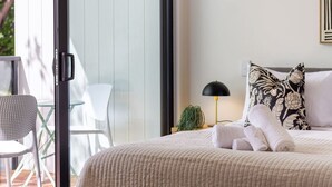 Un dormitorio con cama, mesita de noche, lámpara y vista al exterior.