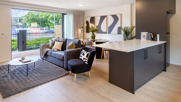 Una sala de estar moderna con un sofá, una mesa de centro y un comedor con una mesa y sillas. Se observa una zona de cocina con armarios y una encimera.