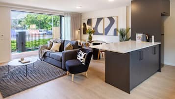 Ein modernes Wohnzimmer mit einer Couch, einem Couchtisch und einem Essbereich mit Tisch und Stühlen. Es gibt eine Küchenzeile mit Schränken und einer Arbeitsfläche.