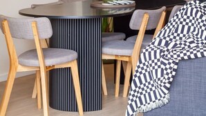 Un comedor moderno con una mesa redonda, cuatro sillas, un jarrón con flores y un aparador oscuro.