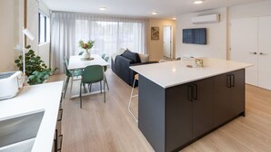 A modern kitchen with a central island, a dining area with a table and chairs, a sofa, and a large window with curtains.